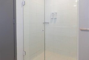 Área de chuveiro com paredes revestidas de azulejos brancos e uma porta.