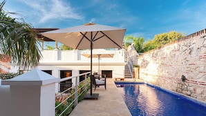 A swimming pool with a stone wall, outdoor furniture, and a pergola with an umbrella. - CASA ESTRADA LUXURY VILLA (Cartagena)
