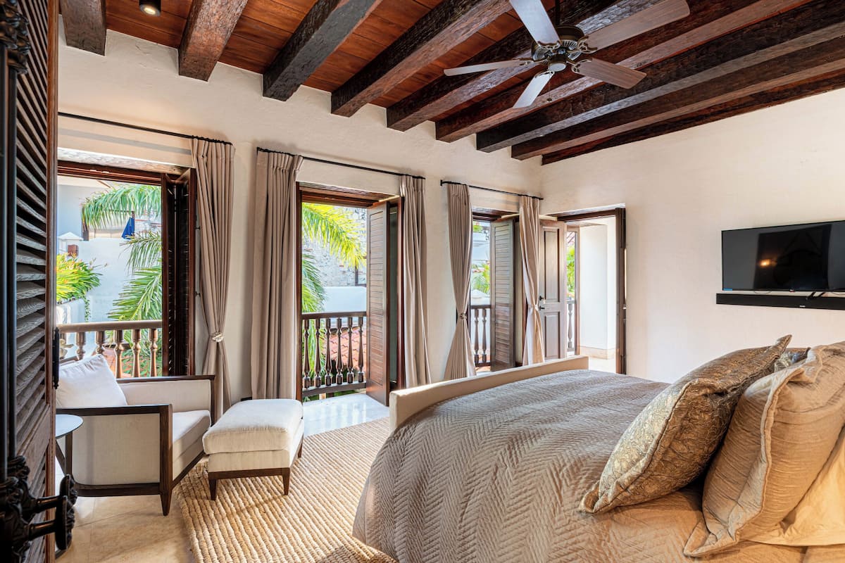 Une chambre avec un grand lit, un ventilateur de plafond et un téléviseur fixé au mur.