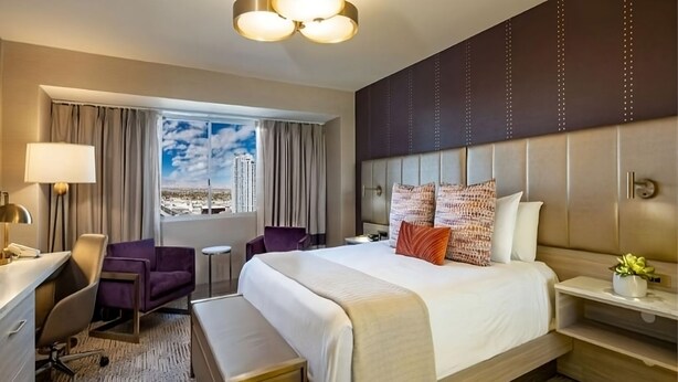 A hotel room with a bed, desk, chair, and a view of the cityscape.