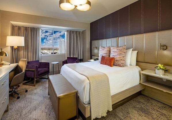 A hotel room with a bed, desk, chair, and a view of the cityscape. - Marra King | Sahara | On the Strip | Free Parking (Las Vegas)