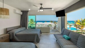 Habitación de hotel con dos camas, un sofá, un televisor y un balcón con vista al océano.