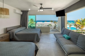 Ein Hotelzimmer mit zwei Betten, einem Sofa, einem Fernseher und einem Balkon mit Blick auf den Ozean.