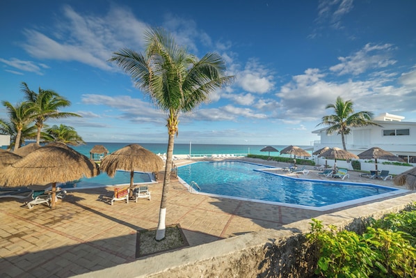 Ein Poolbereich mit Liegestühlen, Palmen und Blick aufs Meer.