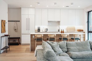 Eine moderne Küche mit weißen Schränken, einer Kaffeemaschine und einem Essbereich mit einer Couch und Stühlen.