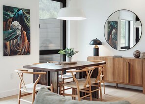 Ein Essbereich mit Holztisch, Stühlen, einer Topfpflanze, einer Lampe und einem Spiegel an der Wand.