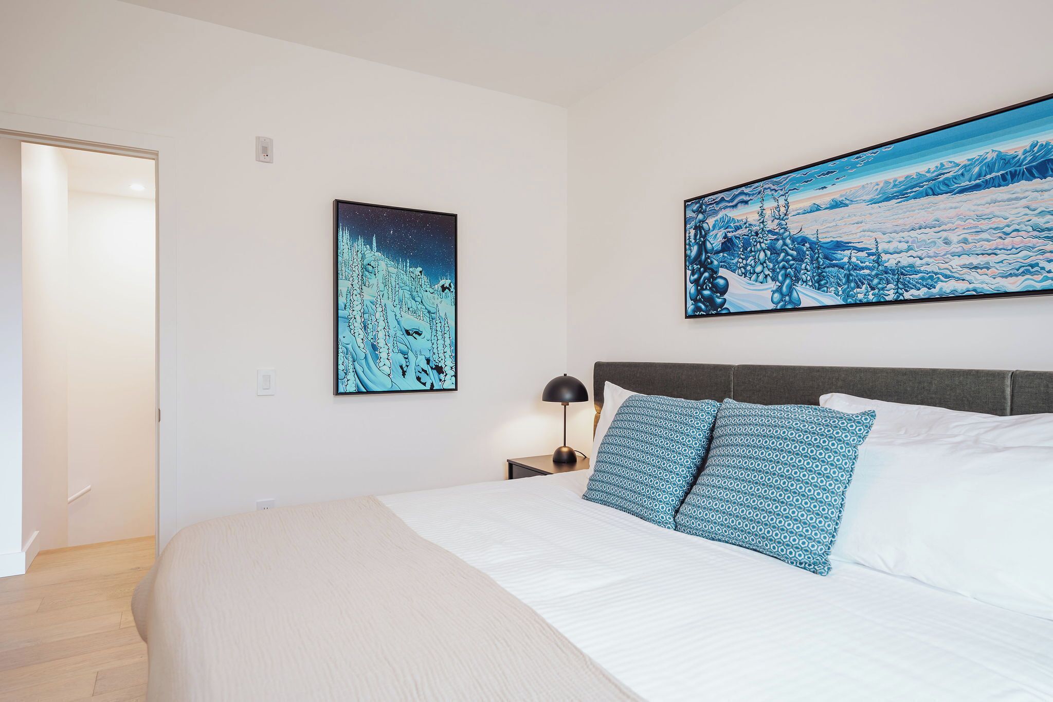 A bedroom with a bed, two pillows, a nightstand, a lamp, and two wall art pieces.