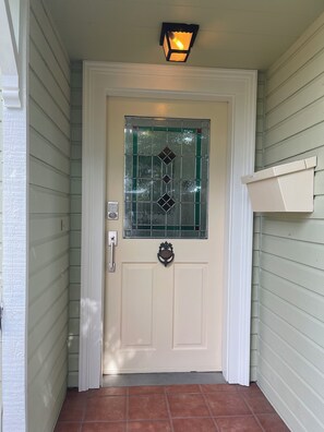 Une porte blanche avec un panneau de verre, un interphone et un luminaire au-dessus.