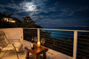 Een balkon met een stoel, een tafel met een fles en glazen, en een kaars.