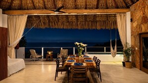 Uma área de refeições com uma mesa posta para quatro pessoas, um ventilador de teto e vista para o mar.