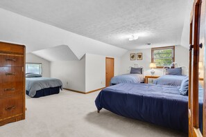Ein Schlafzimmer mit zwei Betten, einer Holzkommode, einem Fenster mit Jalousien und einer Tür.
