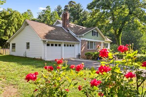 A single-story house with a garage, surrounded by a well-maintained lawn and flowering bushes. - Orchard Ridge Retreat (Flat Rock)