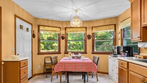 A kitchen with a checkered tablecloth, wooden cabinets, and a chandelier. - Orchard Ridge Retreat (Flat Rock)