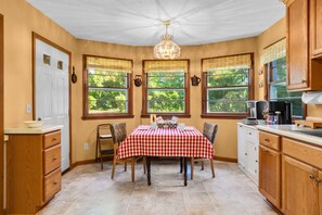 A kitchen with a checkered tablecloth, wooden cabinets, and a chandelier. - Orchard Ridge Retreat (Flat Rock)