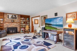 A living room with a fireplace, bookshelves, a TV, a desk with a computer, and a rocking chair. - Orchard Ridge Retreat (Flat Rock)