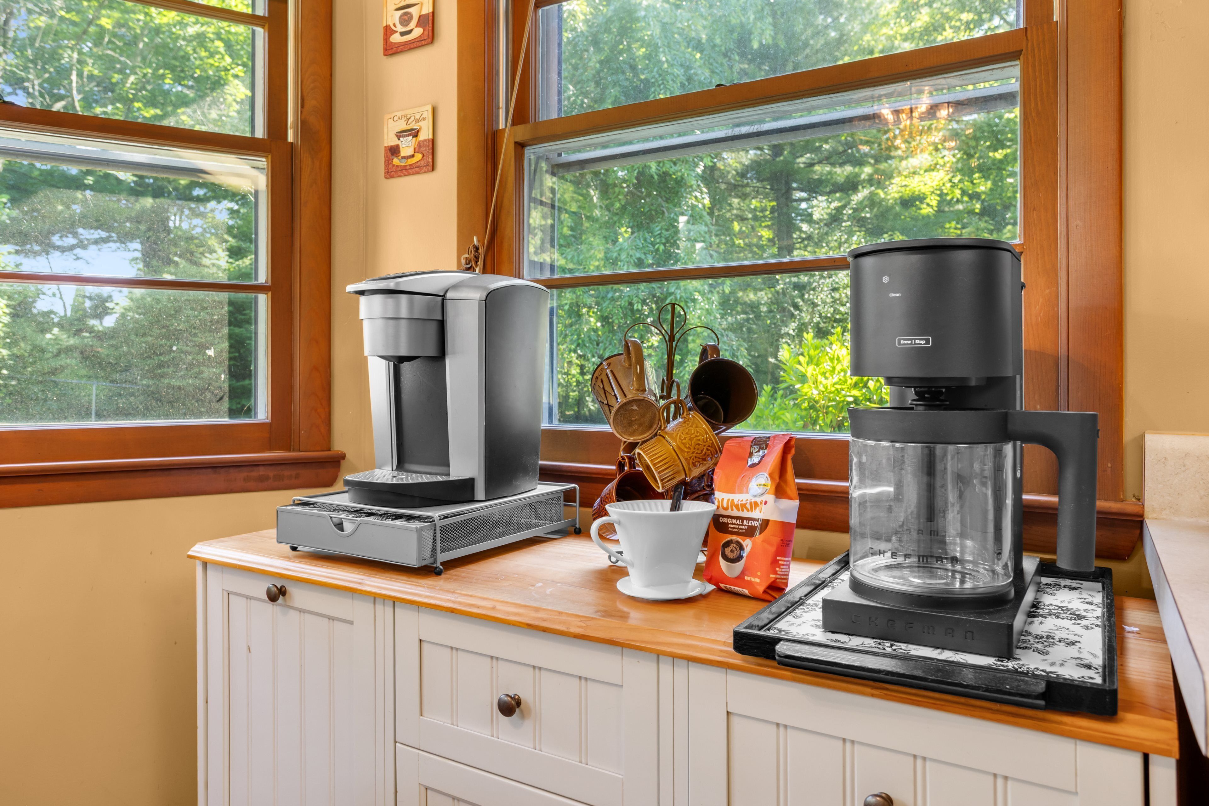 Eine Küchenarbeitsplatte mit Kaffeeautomaten, einer weißen Tasse und einer Packung Dunkin' Donuts Kaffee.