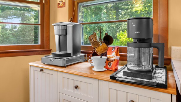 A kitchen counter with coffee makers, a white mug, and a bag of Dunkin' Donuts coffee. - Orchard Ridge Retreat (Flat Rock)