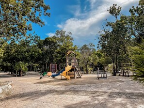 Un'area giochi con scivoli e strutture per arrampicarsi, circondata da alberi e un cielo sereno.
