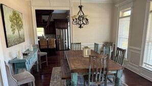 Un comedor con una mesa y sillas de madera, una araña y un cuadro en la pared.