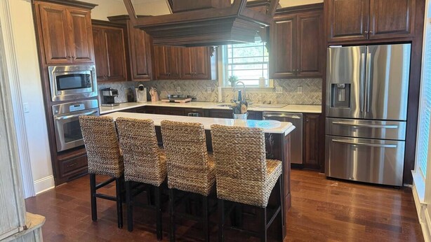 Una cocina con armarios de madera, electrodomésticos de acero inoxidable, una zona de bar con sillas de mimbre y un backsplash de baldosas tipo espiga.