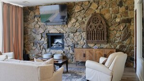 A stone-walled living room with a fireplace, a flat-screen TV, and a wooden cabinet. - Welcome to 30A Glass House — a bright, modern coastal retreat (Santa Rosa Beach)