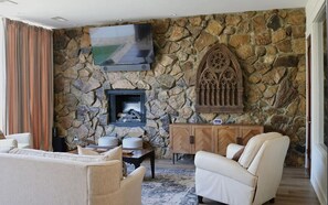 A stone-walled living room with a fireplace, a flat-screen TV, and a wooden cabinet. - Welcome to 30A Glass House — a bright, modern coastal retreat (Santa Rosa Beach)