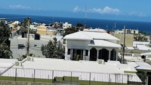 A coastal residential area with buildings, a white-roofed house, and a clear view of the ocean. - 2BR Apartment with Ocean & Mountain Views (Puerto Plata)