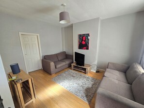 A living room with a sofa, a television on a stand, a rug, and a painting on the wall. - Belfast Diggs (Belfast)