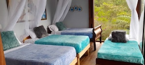 A room with two beds, a window with a view of greenery, and a mosquito net.