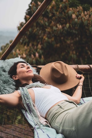 A person lying on a hammock outdoors with a hat and a blanket.
