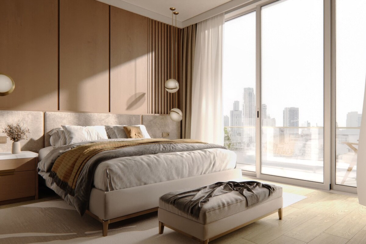 A modern bedroom with a large bed, bedside tables, a bench, and a city view.