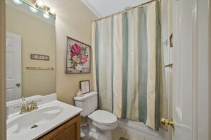Um banheiro com pia branca, vaso sanitário, quadro com flores e cortina de chuveiro listrada.
