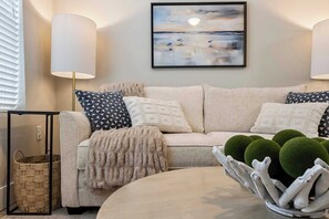 Un salon comprenant un canapé, des coussins à motifs, un tableau encadré et un bol décoratif contenant des sphères vertes.