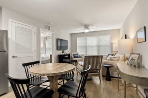 A modern living room with a round wooden table, black chairs, a sofa, and a TV mounted on the wall. - Down The Shore Condo | Jersey Meets Bama (Tuscaloosa)
