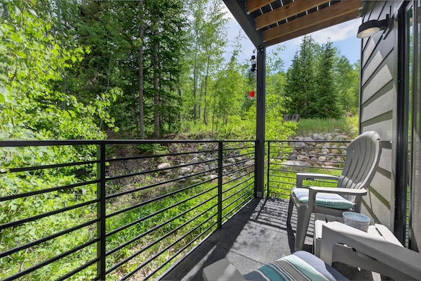 Ein Balkon mit Blick auf einen Wald, einem Metallgeländer und zwei mit Kissen ausgestatteten Stühlen.