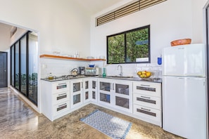 Eine moderne Küche mit weißen Schränken, einem eingebauten Backofen, einem Kühlschrank und einem Fenster mit Blick auf Grünflächen.