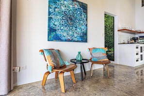 Ein modernes Wohnzimmer mit zwei Holzstühlen, einem runden Tisch und einem großen blauen Mandalamalerei an der Wand.
