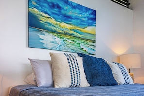 Ein Bett mit einem gemusterten Überwurf, zwei Kissen und einem Wandbild mit einer Strandansicht.