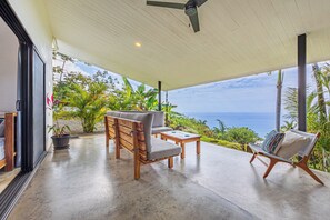 Ein überdachter Außenbereich mit Meerblick, Holzmöbeln und einem Deckenventilator.