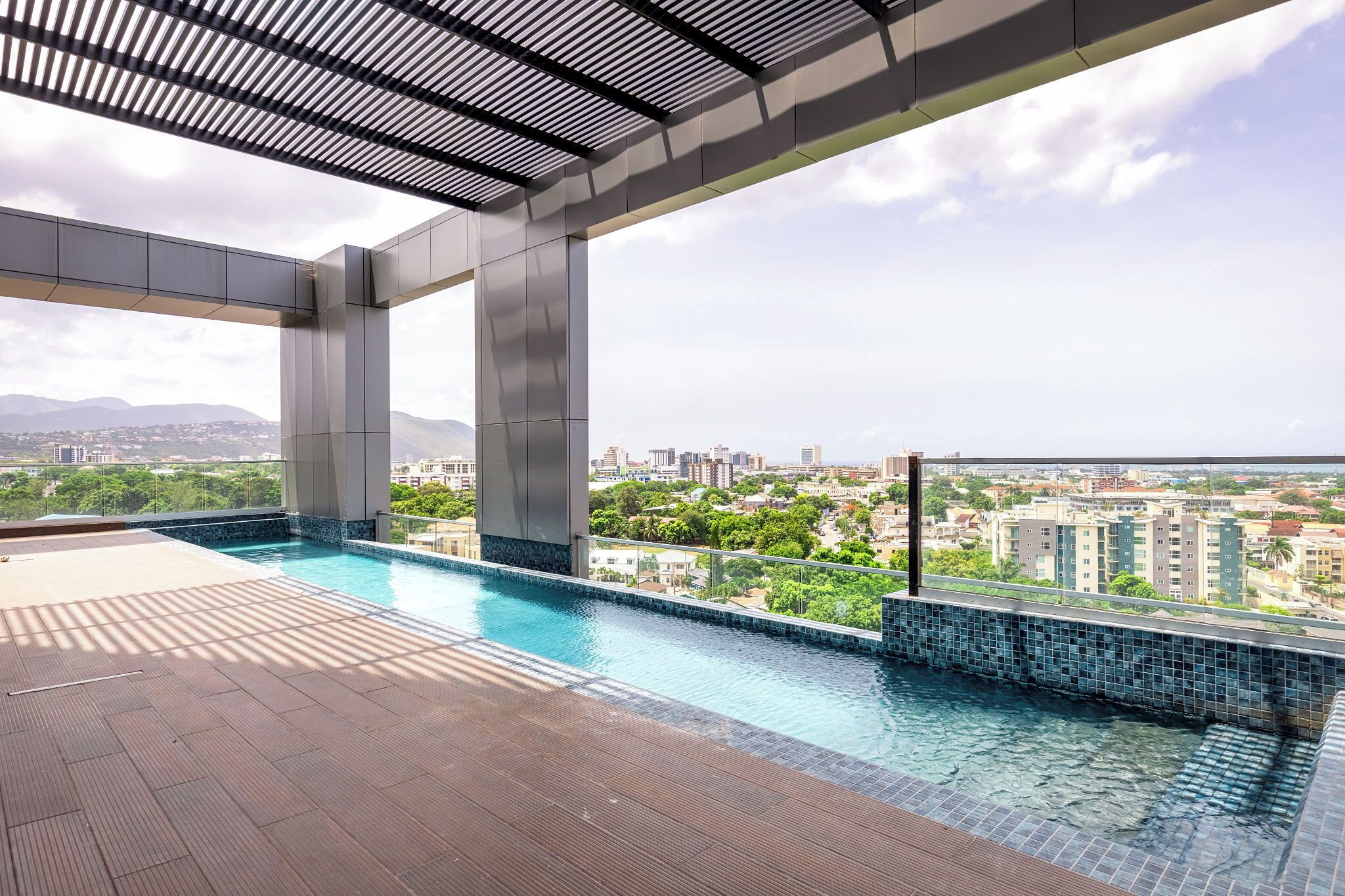 A rooftop infinity pool with a city view, surrounded by a wooden deck and metal beams.