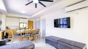 A modern living room with a sofa, a dining table with chairs, a ceiling fan, and a flat-screen TV mounted on the wall.