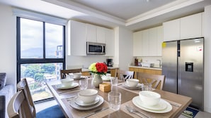 Eine moderne Küche mit Edelstahlgeräten, ein Essbereich mit Tisch für vier Personen und Blick auf die Stadt durch große Fenster.