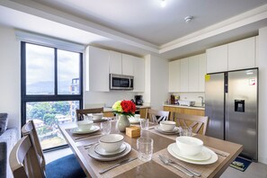 A modern kitchen with stainless steel appliances, a dining area with a table set for four, and a view of the city through large windows. - Heart of New KGN/Gated/TV/Wifi/AC/Pool/Embassies (Kingston)