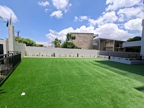 A well-maintained lawn with a stone wall and modern buildings in the background. - Heart of New KGN/Gated/TV/Wifi/AC/Pool/Embassies (Kingston)