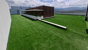 Eine Dachterrasse mit künstlichem Gras, einer Holzkonstruktion und Blick auf ferne Berge.