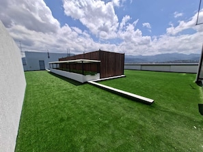 A rooftop terrace with artificial grass, a wooden structure, and a view of distant mountains. - Heart of New KGN/Gated/TV/Wifi/AC/Pool/Embassies (Kingston)
