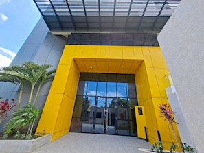 A modern building entrance with a yellow facade, large glass doors, and a covered entrance area. - Heart of New KGN/Gated/TV/Wifi/AC/Pool/Embassies (Kingston)