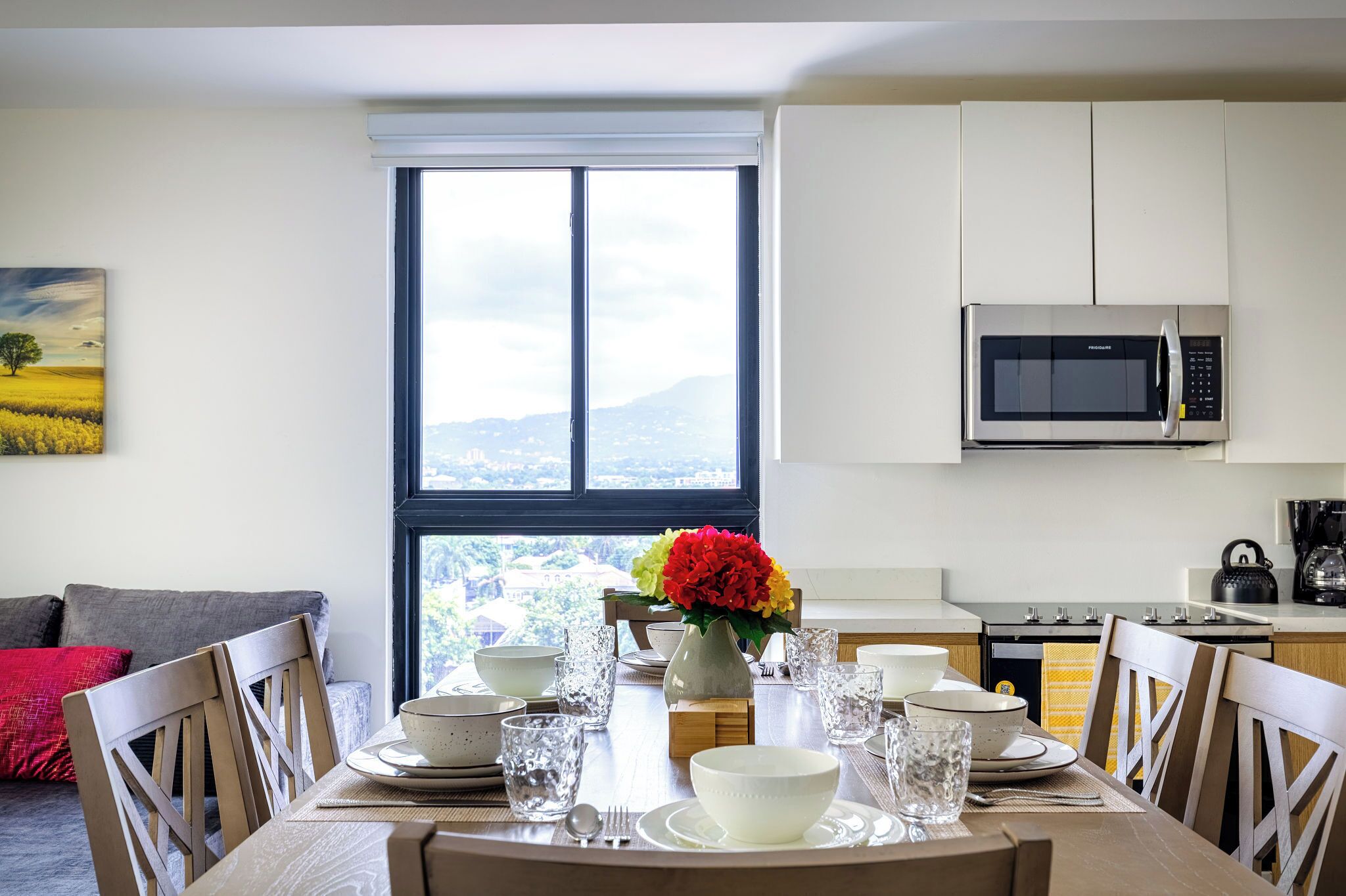 A dining area with a table set for four, a window with a view, and a kitchen with a microwave.