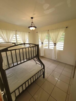 A room with a bunk bed, large windows with curtains, a tiled floor, and a hanging light fixture. - The Villa in Miradero (Mayaguez)