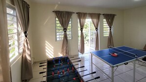 Ein Zimmer mit Kicker, Tischtennisplatte und fensterbelaubten Fenstern.